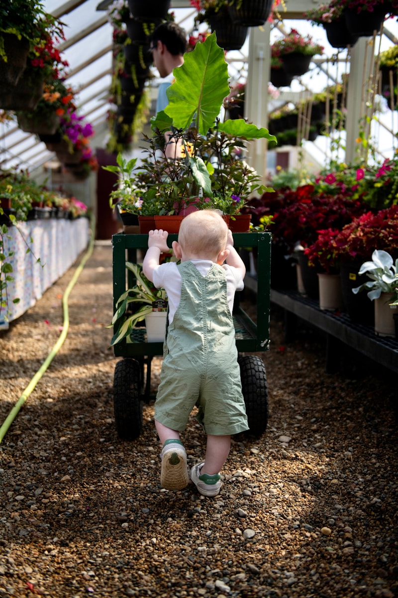 a baby in overalls pushing a cart with plants in it